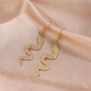 Boucles d'oreilles serpent dorées avec yeux en strass bleus sur satin de soie champagne