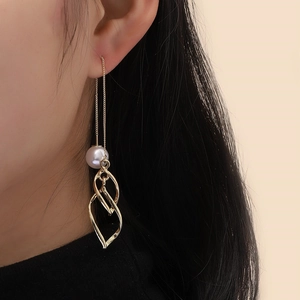 Detail showing long gold tassel earring with white pearl and leaf pendants on model