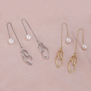 Close-up of elegant gold and silver pearl drop earrings on smooth pink silk fabric