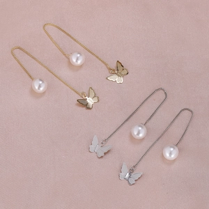 Detailed close-up of gold and silver butterfly pearl drop earrings on silk