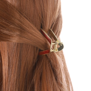 Detail view of the golden V-shaped hair claw clip with red enamel on long brown hair