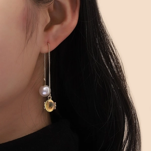 Detail of long gold chain earrings with pearls and amber stones on female model
