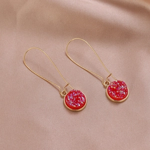 Dettaglio macro di orecchini in resina rossa con glitter scintillanti su seta champagne