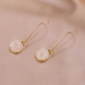 Dettaglio macro di orecchini a goccia tondi in resina druzy rosa con gancio dorato