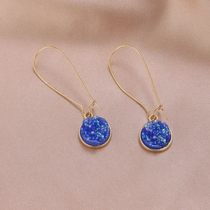 Dettaglio di orecchini pendenti in oro con cristalli tondi in resina druzy blu scuro