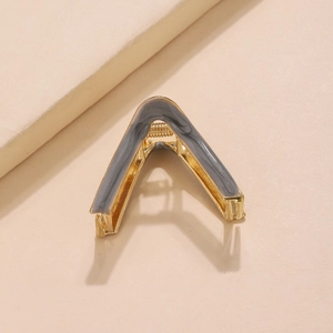 Close-up of golden V-shaped metal hair claw with grey marble pattern inlay on beige base