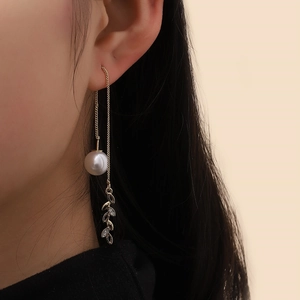 Detail view of long gold tassel earrings with pearl and shimmering leaf charm