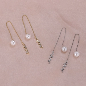 Close-up of gold and silver tassel earrings with leaf charms and round white pearls