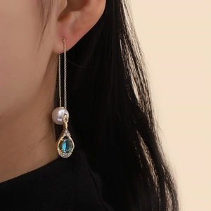 Detailed close-up of a long gold chain earring featuring a white pearl and blue sapphire droplet