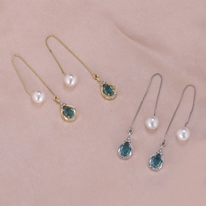 Detailed view of long gold and silver drop earrings with blue zircon and pearls