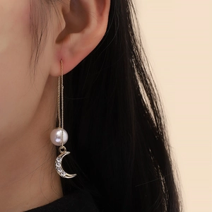 Close-up of elegant gold tassel earrings with pearl and moon pendant on model