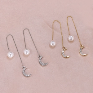 Detailed view of gold and silver moon pearl drop earrings on pink silk background