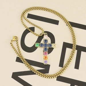 Detailed close-up of golden cross pendant with colorful zircon stones on box chain