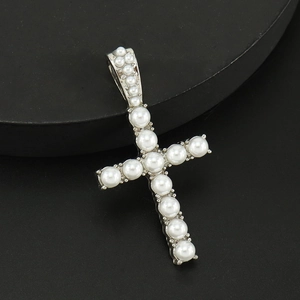 Detalle de un colgante de cruz plateado con perlas blancas sobre fondo negro mate