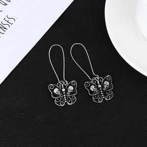Gothic butterfly drop earrings with black wings and silver skull accents on a dark background