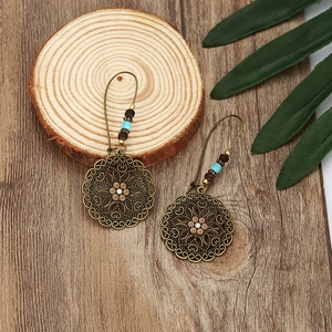 Bohemian style hollow flower drop earrings with turquoise beads on a rustic wooden base