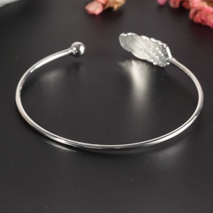 Close-up of silver-tone open cuff bracelet with feather and bead details on dark background