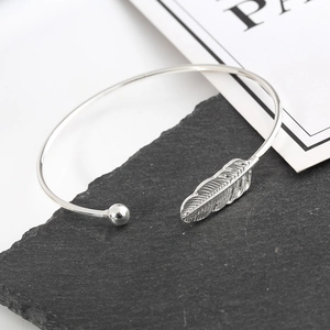 Macro detail of silver open bangle featuring textured feather and polished bead accents