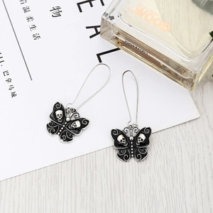 Gothic butterfly earrings with black enamel and silver skull charms on white background