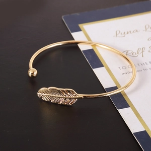Close-up of golden feather open cuff bracelet with small bead detail on dark background