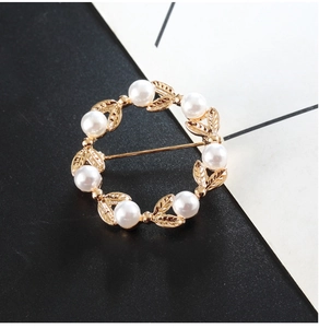 Détail d'une broche circulaire à feuilles dorées et perles blanches sur un fond bicolore