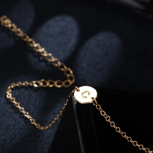 Macro shot of gold charm bracelet featuring a polished circular pendant with letter C