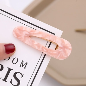 Close-up of pink marble pattern acetate hair clip with hollow oval design and gold metal clip