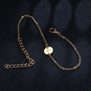 Macro view of gold chain bracelet featuring a round pendant with engraved letter G