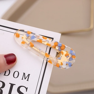 Detail shot of a golden metal hair clip featuring a colorful resin terrazzo pattern