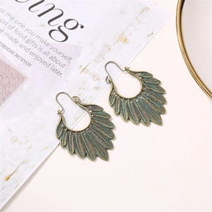 Detailed close-up of antique bronze feather earrings with green patina on a white background