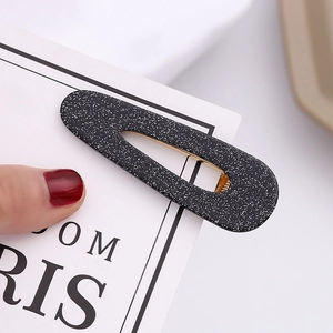 Close-up of black resin waterdrop hair clip with white glitter stars and golden metal clip