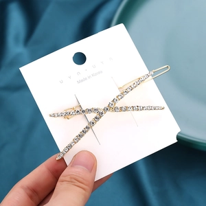 Elegant gold X-shaped hair clip with sparkling white rhinestones on silk background