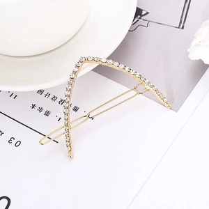 Macro detail of a golden V-shaped hair clip with shimmering rhinestones and metal bar