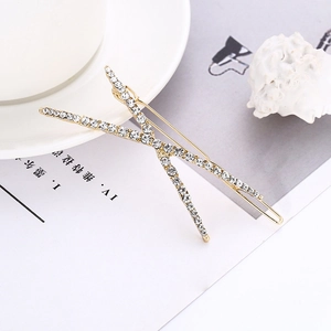 Close-up of golden X-shaped hair clip with sparkling white rhinestones on art magazine