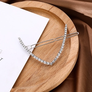 Detail of V-shaped silver metal hair clip with sparkling rhinestones on a wooden tray