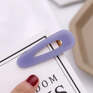 Close-up of a purple matte teardrop hair clip with golden metal clip on a display card