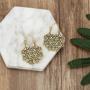 Vintage gold hollow geometric earrings with mandala patterns on marble and wood surface