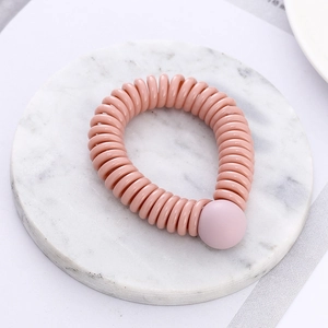 Pink spiral telephone wire hair tie with decorative bead on marble surface