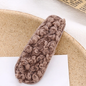 Fermaglio per capelli BB in lana di agnello marrone con morbida texture riccia su piatto