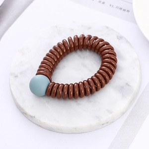 Brown spiral telephone wire hair tie with a light blue bead on marble background
