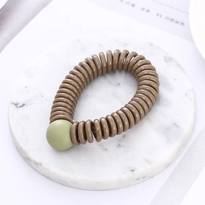 Detail of a brown spiral telephone wire hair tie with a matte green decorative bead