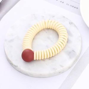 Detail of a creamy white spiral hair tie with a matte red bead on a marble tray