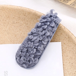 Dettaglio di un fermaglio per capelli in peluche riccio grigio-blu su vassoio di sughero