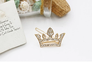 Detail view of a gold crown hair clip with sparkling white rhinestones on shell background