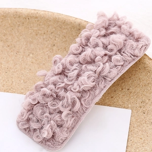 Close-up of pink-purple curly plush rectangular hair clip on a warm wooden tray