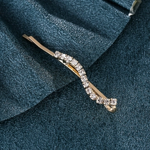 Elegant gold wave-shaped hair clip with sparkling rhinestones on blue fabric