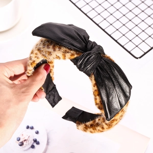 Handheld leopard print plush headband with a large black faux leather bow accent
