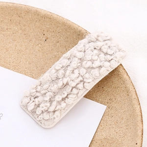 Close-up of cream fuzzy plush rectangle BB hair clip on a ceramic plate decor