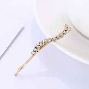 Elegant gold-plated hair clip with sparkling transparent crystals on a white ceramic dish