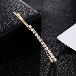 Close-up of a golden bobby pin with crystal rhinestones on a dark textured surface